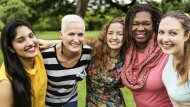 a group of smiling happy women standing together outdoors in a row with their arms around one anothers shoulders 16X9